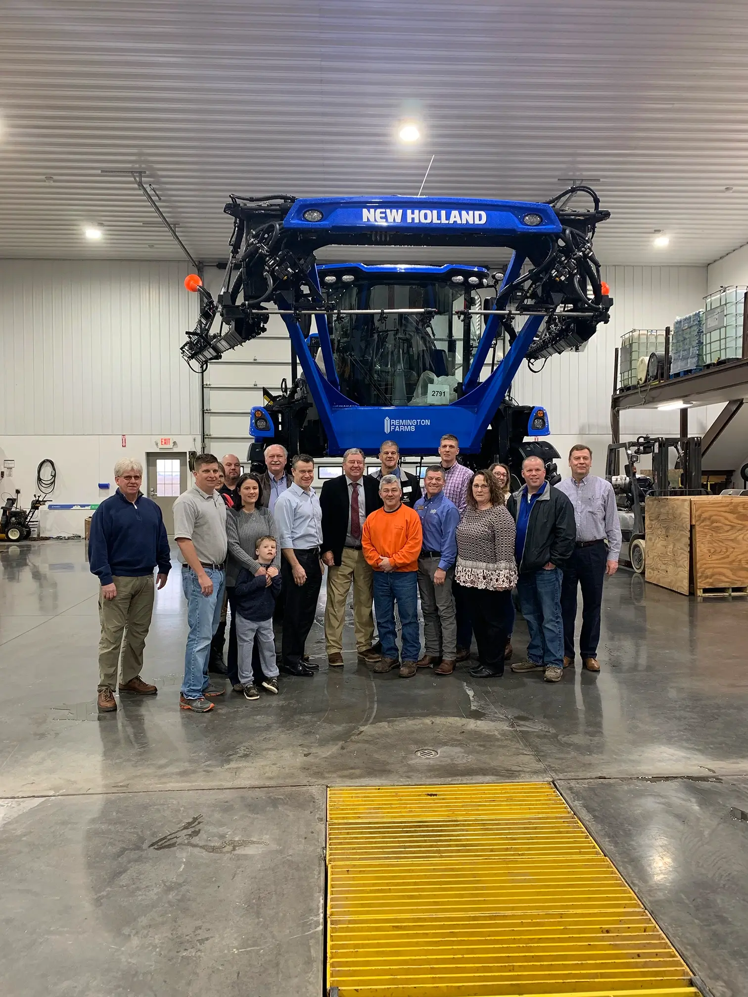 A group of people gathered around a New Holland sprayer